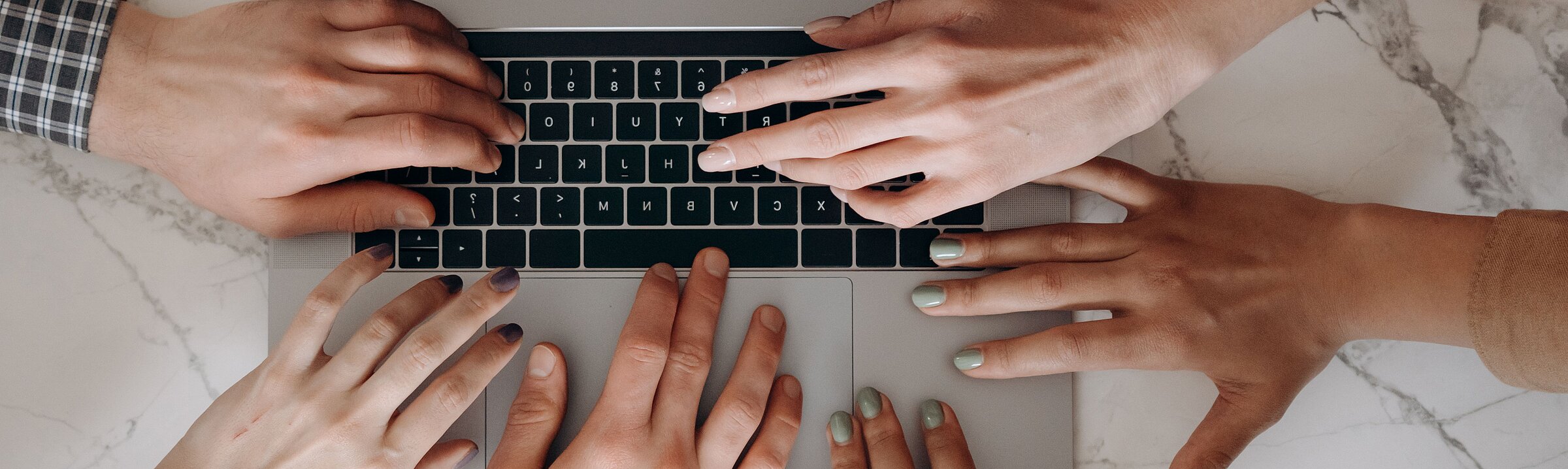 Verschiedene Hände über einem Laptop als Symbol für digitale Vielfalt.