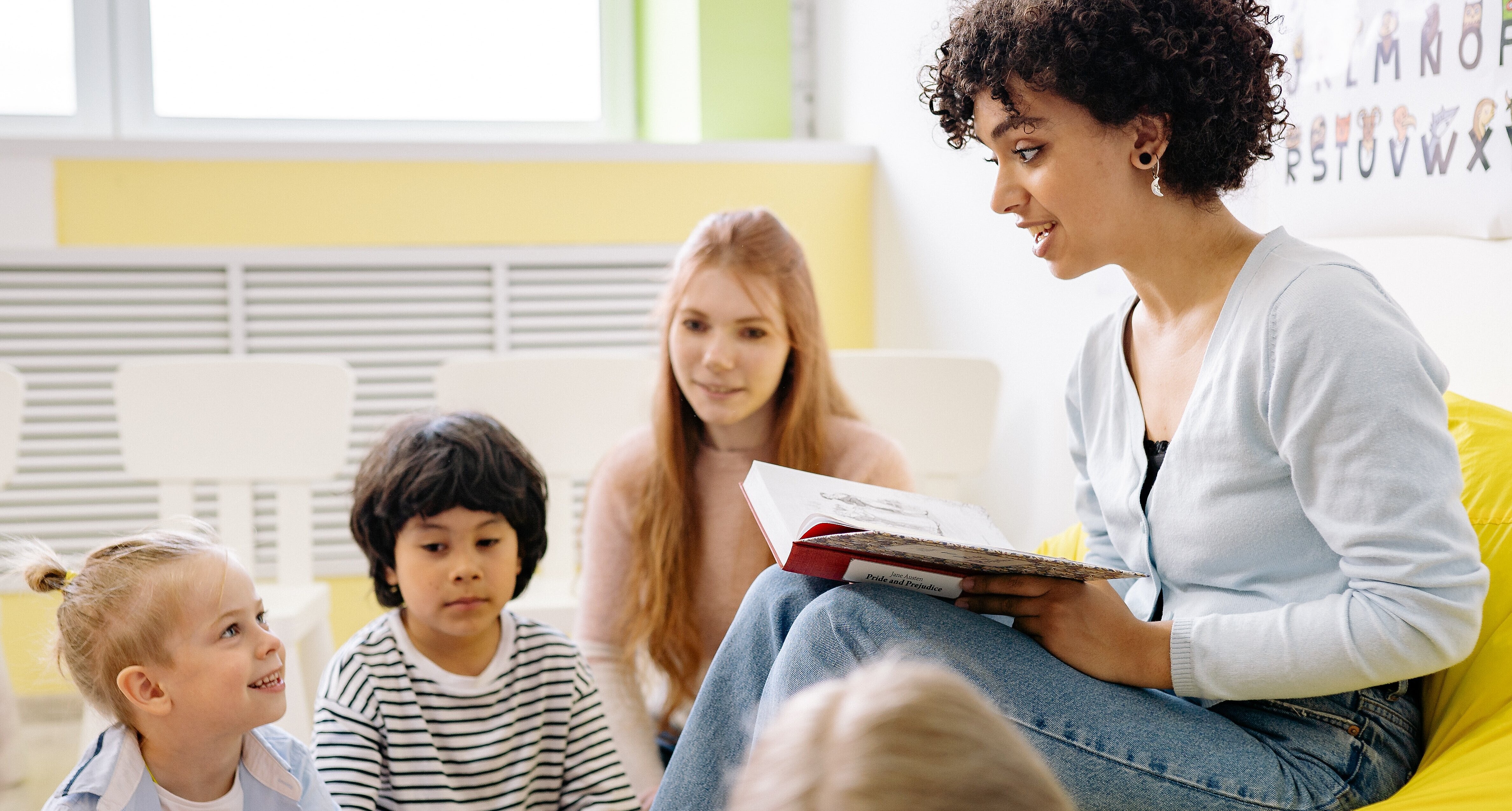 Symbolfoto Unterricht Lehrer:in die Kindern auf Sofa vorliest