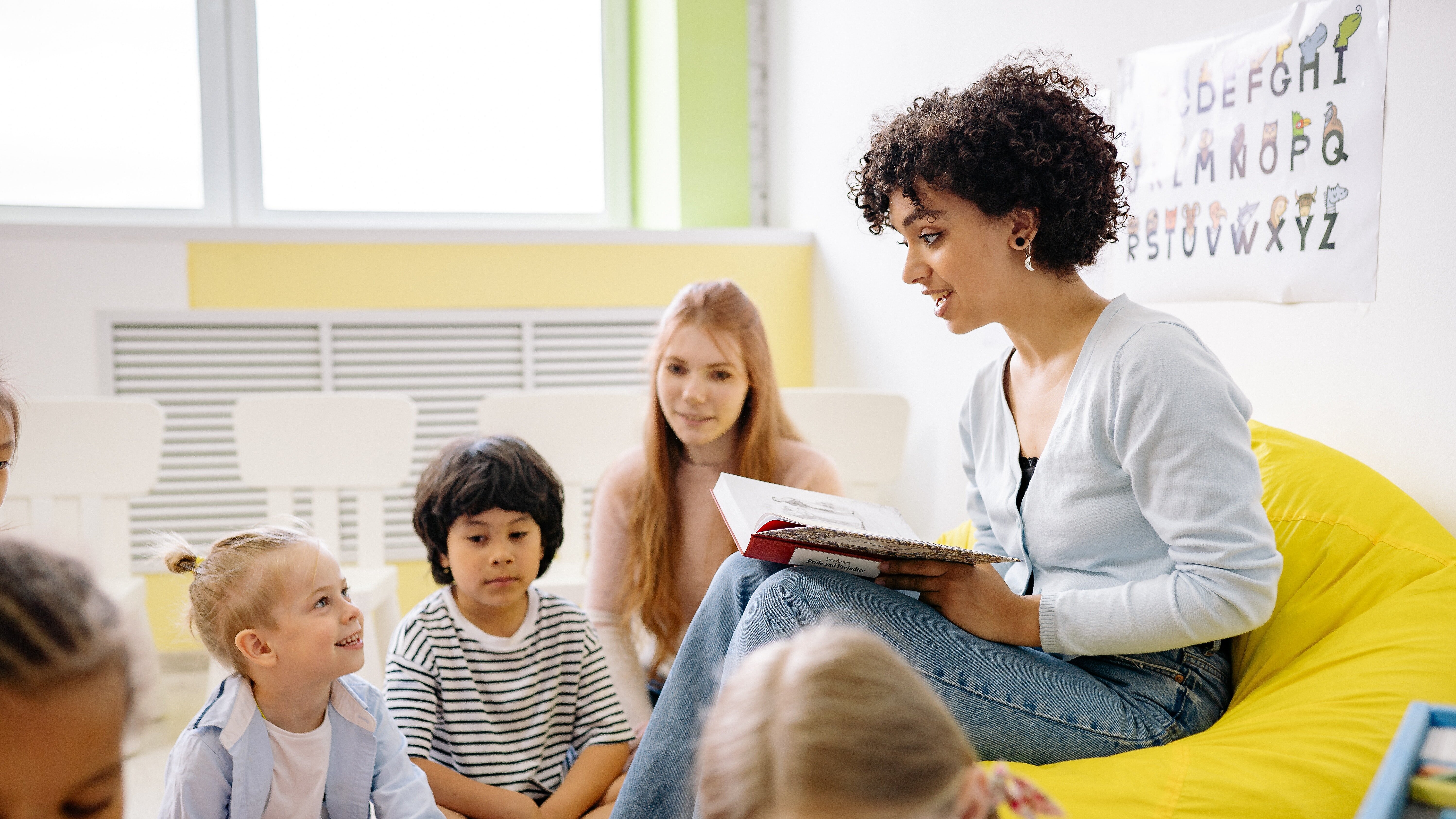 Symbolfoto Unterricht Lehrer:in die Kindern auf Sofa vorliest