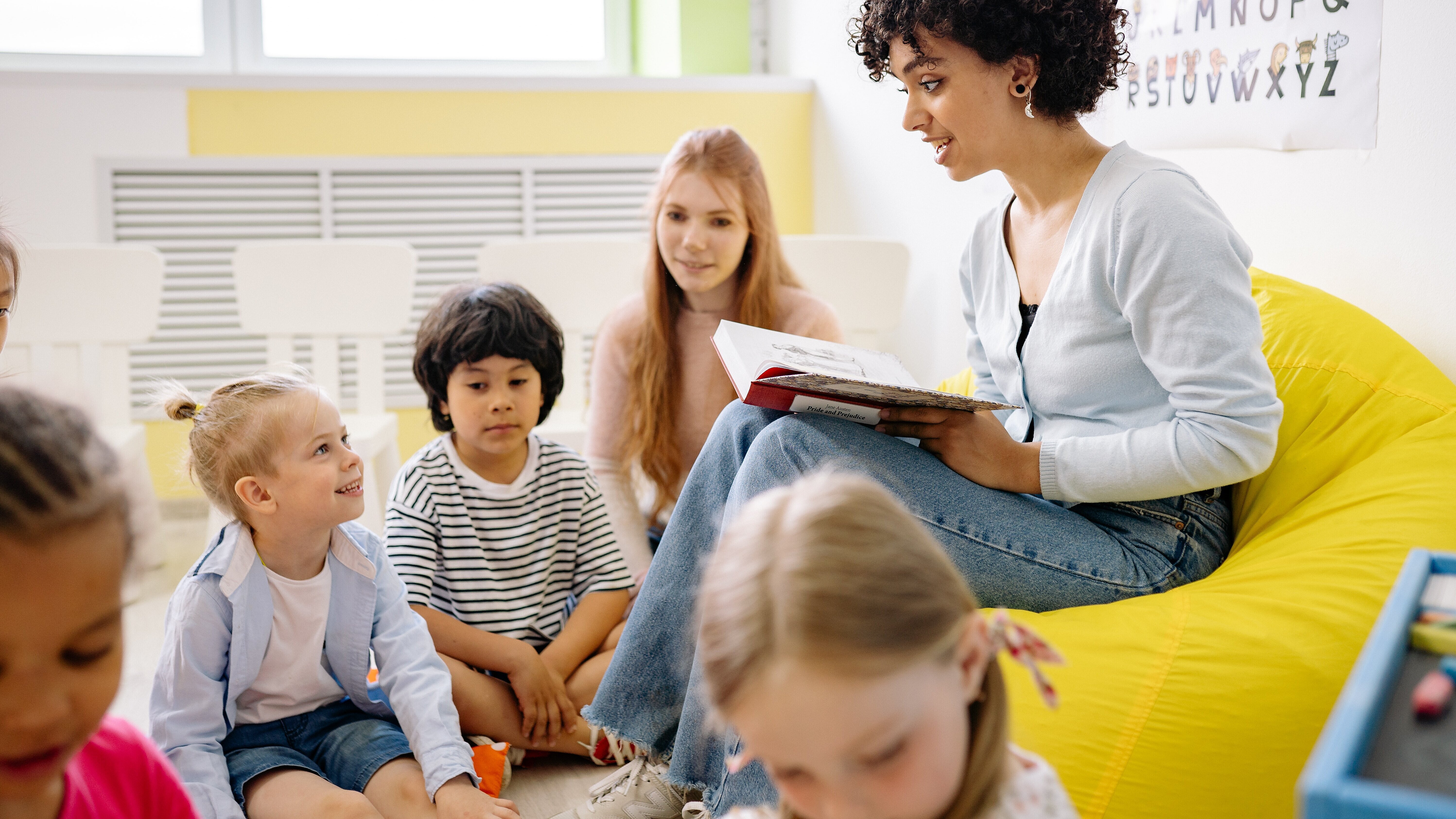 Symbolfoto Unterricht Lehrer:in die Kindern auf Sofa vorliest