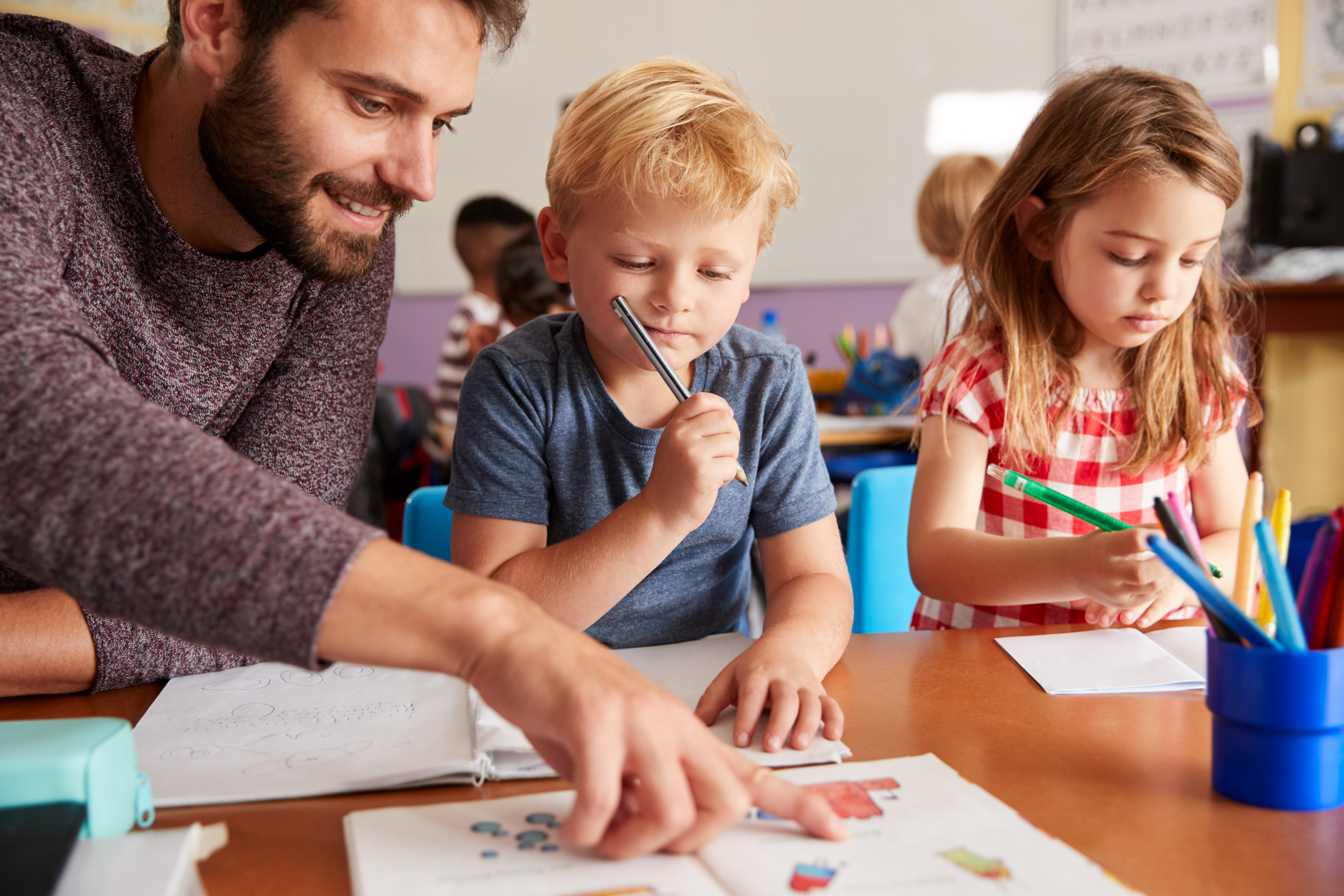 Symbolfoto Lehrer:in mit Schüler:innen am Tisch