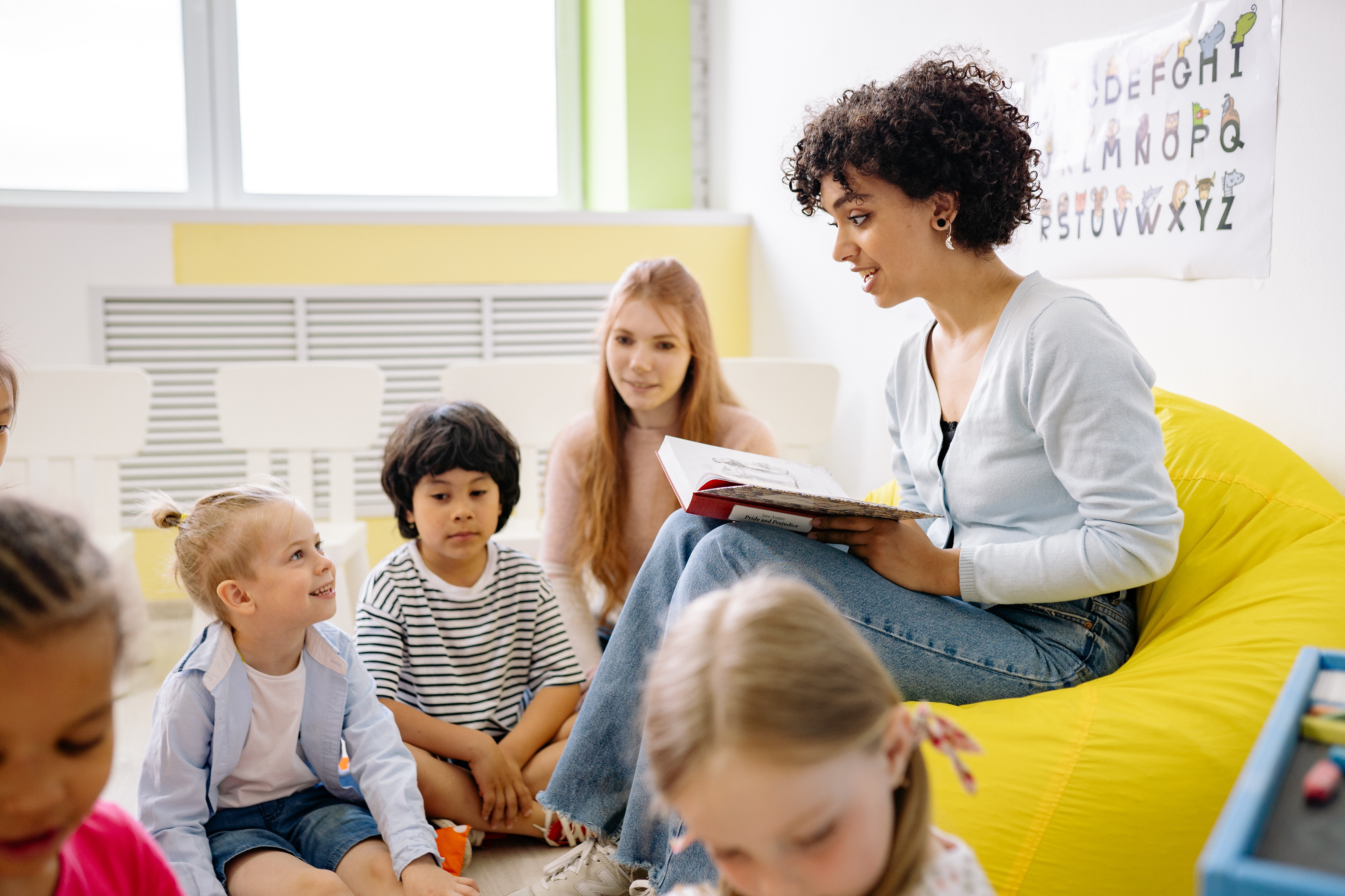 Symbolfoto Unterricht Lehrer:in die Kindern auf Sofa vorliest